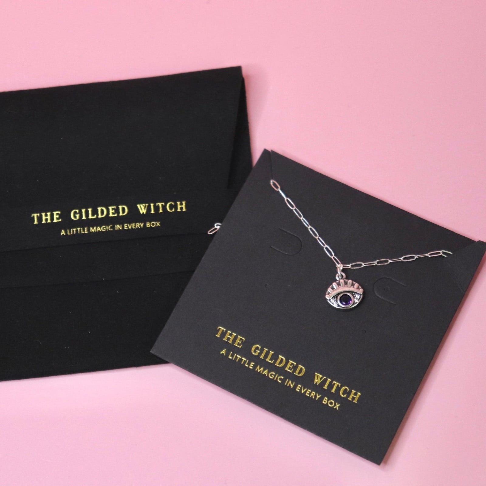 The Sterling Silver Purple Evil Eye Necklace with Paperclip Chain on a pink background.