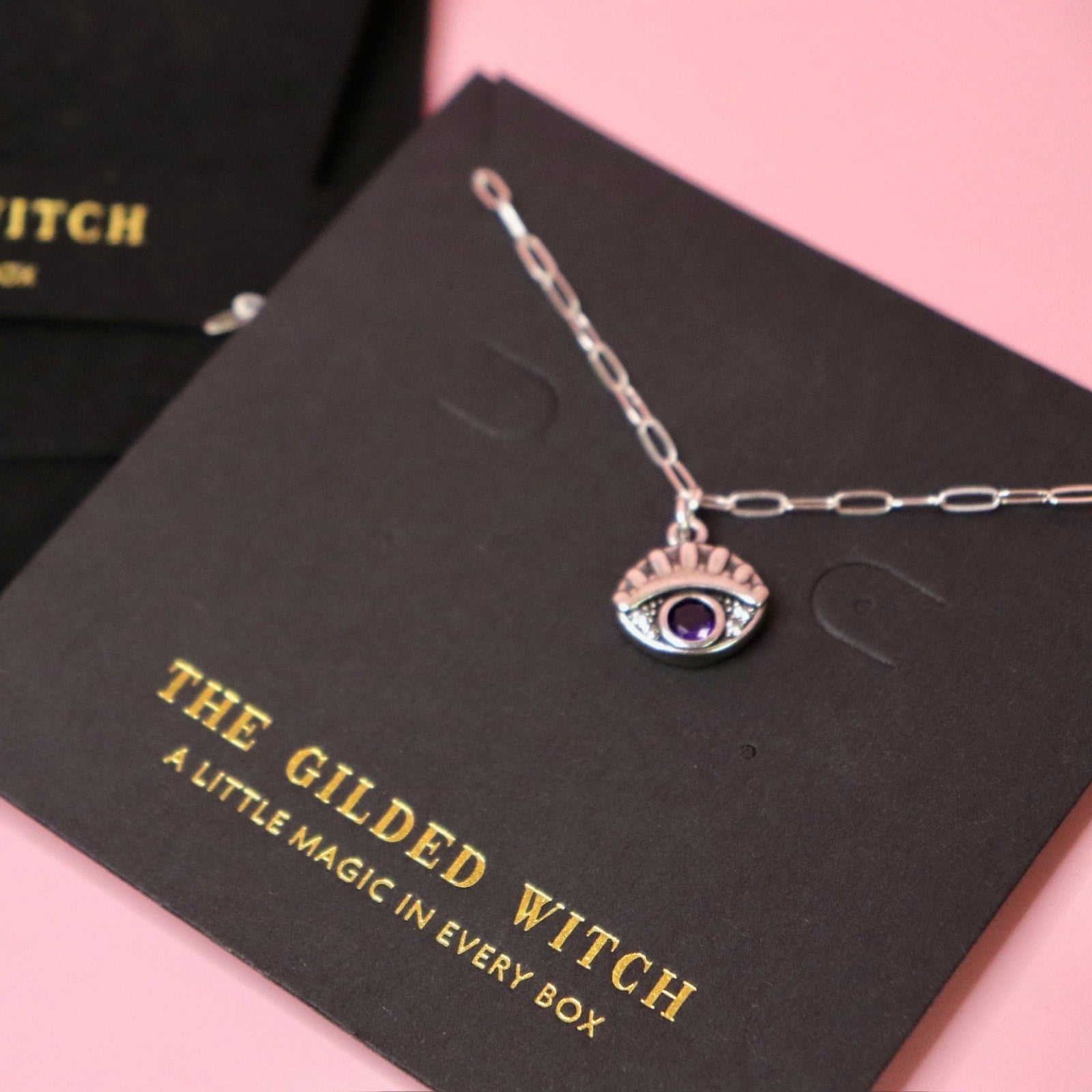 The Sterling Silver Purple Evil Eye Necklace with Paperclip Chain on a pink background.