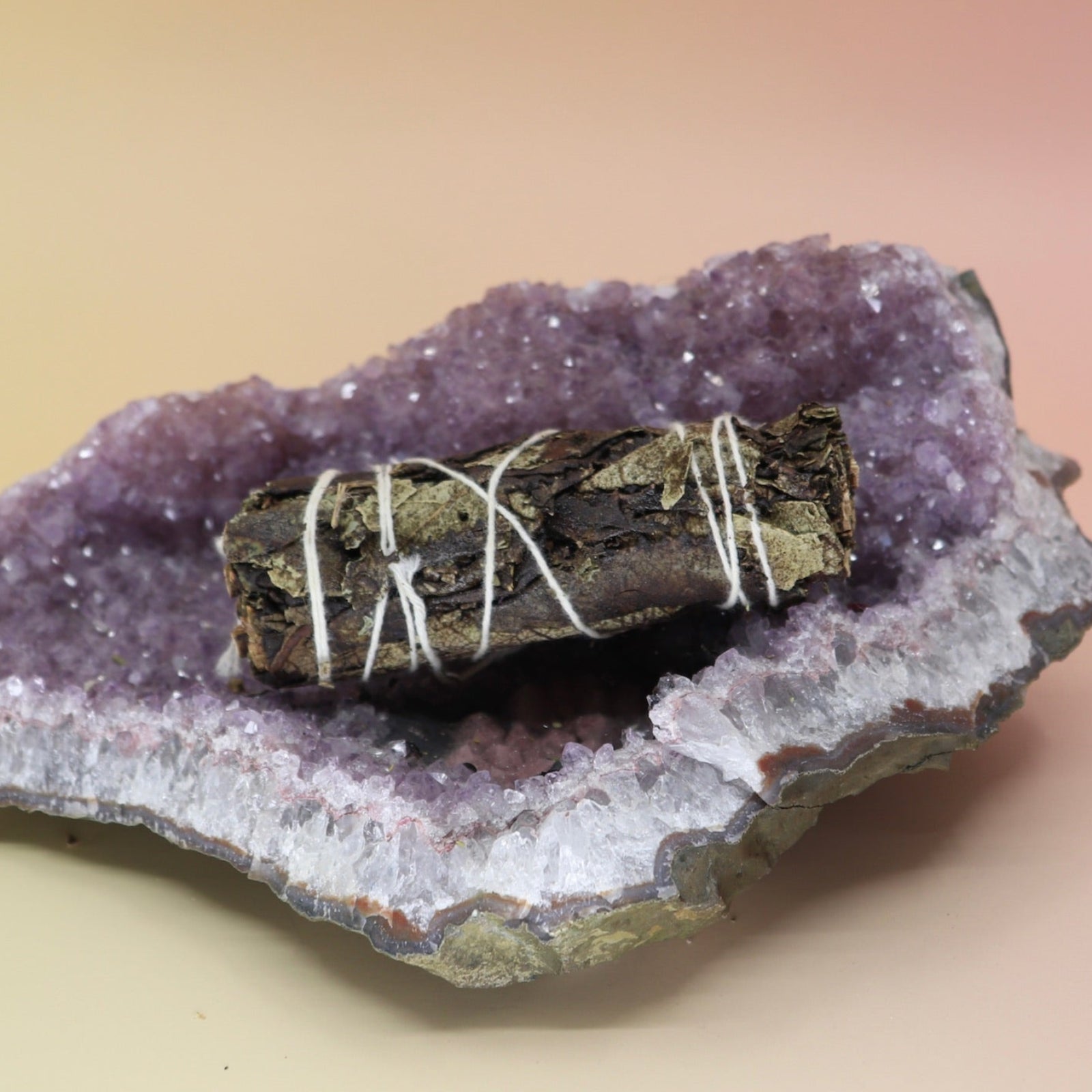 The Organic Black Sage - 4 in. Smudge Stick on an amethyst piece all on a pink and yellow background.