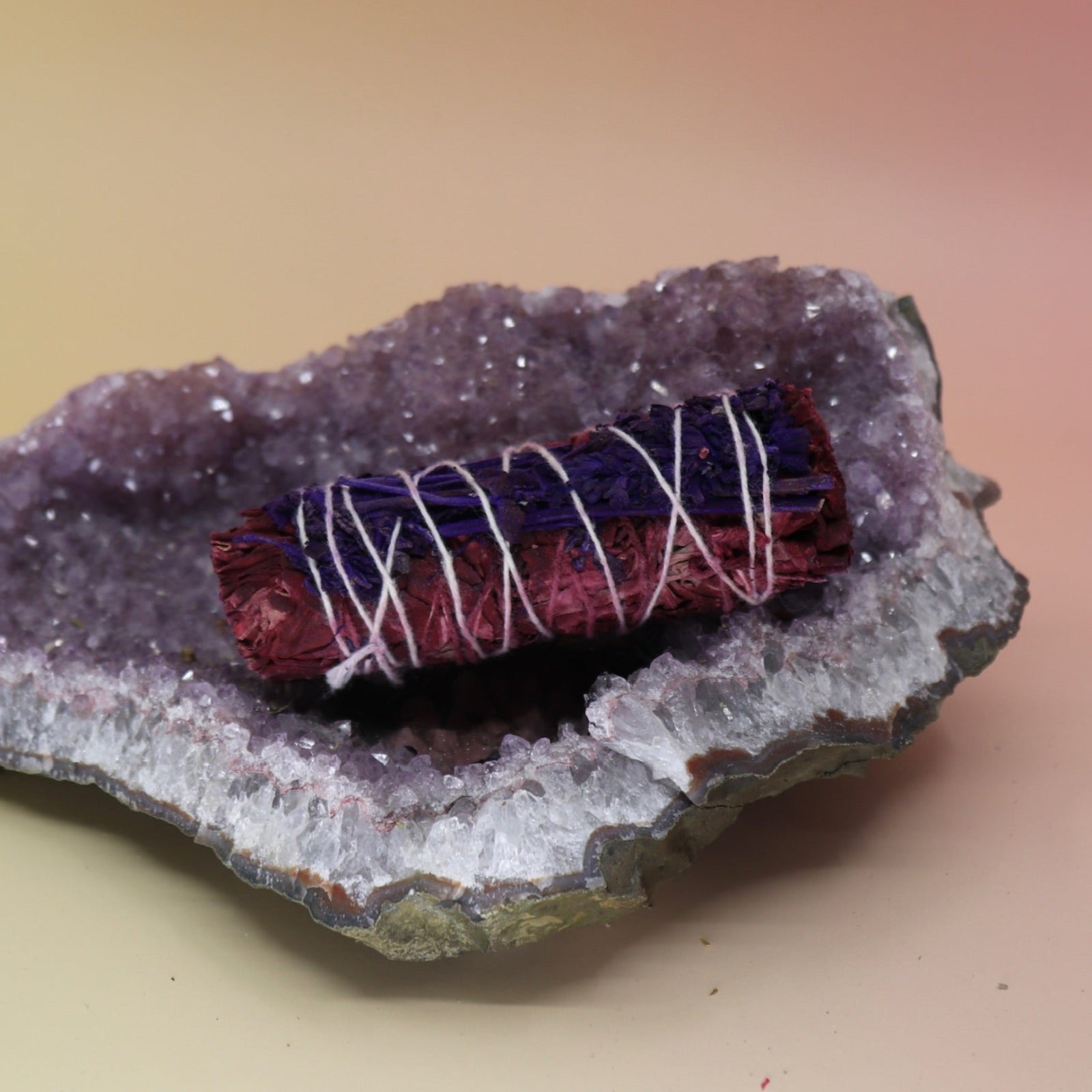 The Dragon Blood Sage with Lavender - 4 in. Smudge on an amethyst piece all on a pink and yellow background.