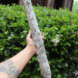 Someone holding the Jumbo Organic California White Sage - 20" Sage Smudge Stick in front of a green bush.