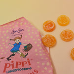 The Pippi Longstocking Gold Coins bag lying on a yellow surface with candies to the right of it.