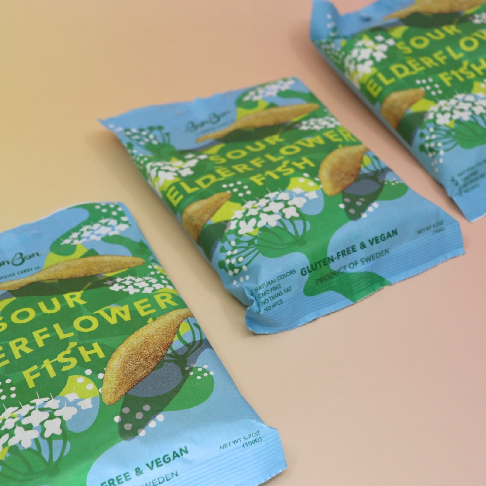 Three bags of the BonBon NYC Sour Elderflower Fish - Swedish Candy on a pink and yellow background.