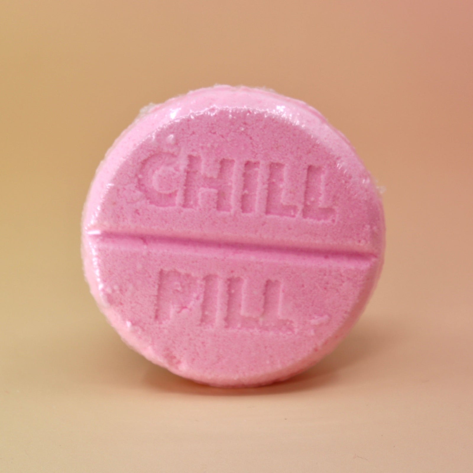 The Chill Pill Bubble Bath Bomb on a peach colored background.