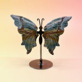 The Natural Marine Jasper Butterfly Crystal with Stand on a pink and yellow background.