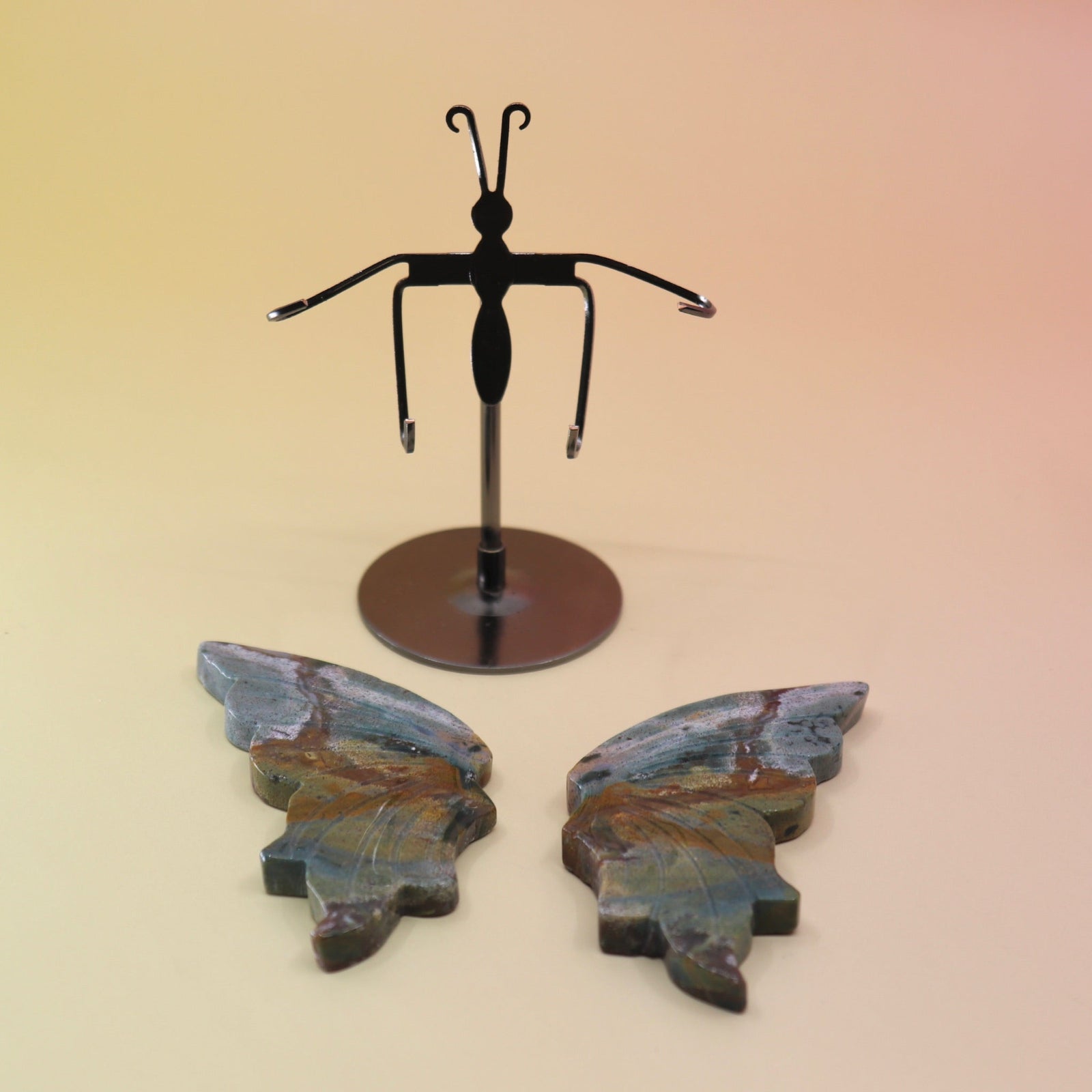 Two of the Natural Marine Jasper Butterfly Crystal with Stand on a pink and yellow background with the crystal butterfly wings off the stand.