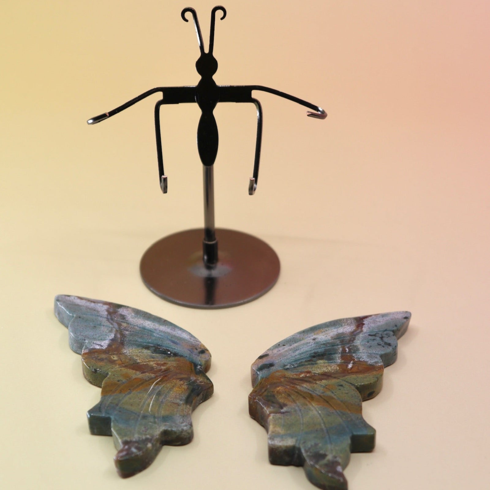 Two of the Natural Marine Jasper Butterfly Crystal with Stand on a pink and yellow background with the crystal butterfly wings off the stand.