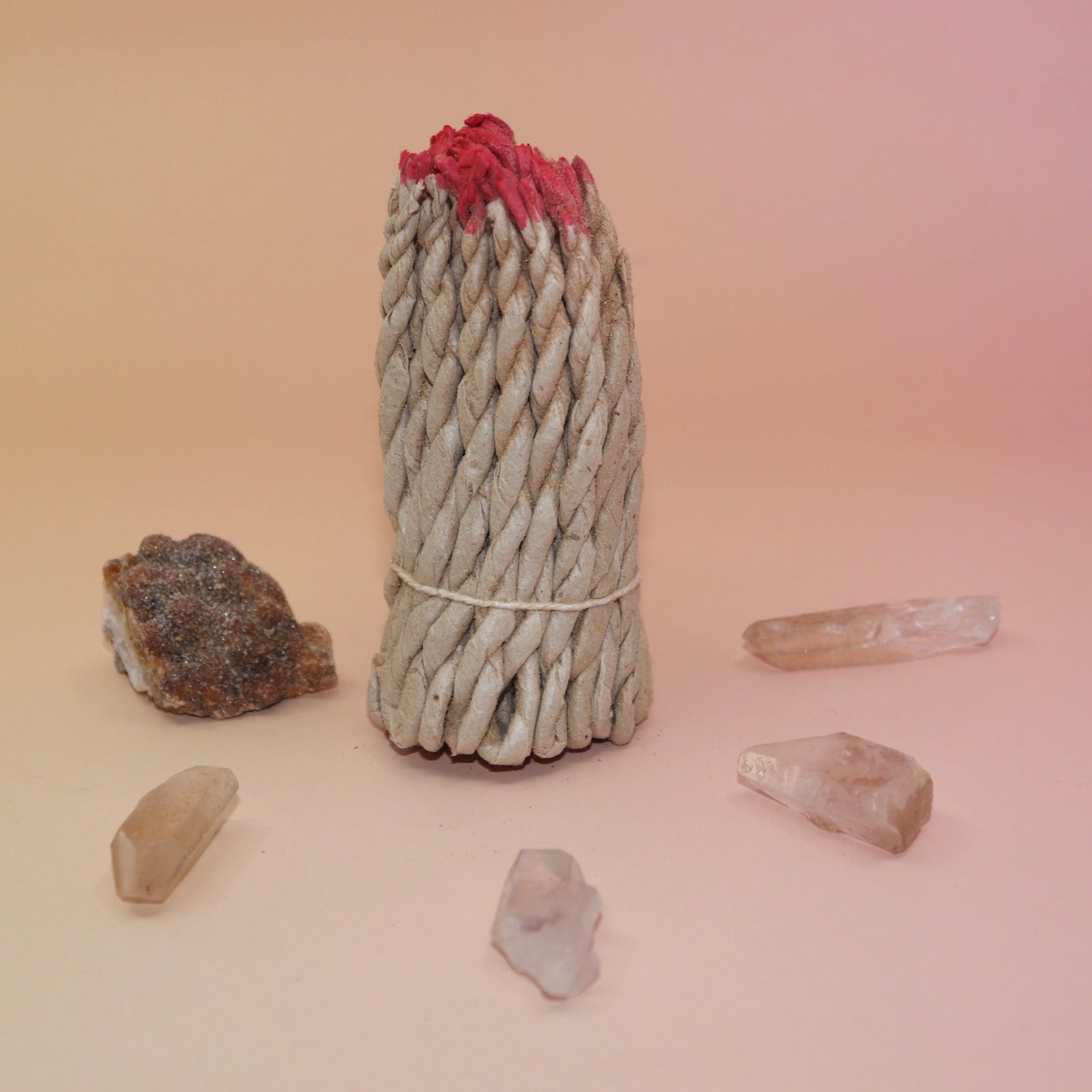 The Nepalese Himalayan Hand Rolled Incense Ropes with crystal points surrounding it all on a light pink and yellow background.
