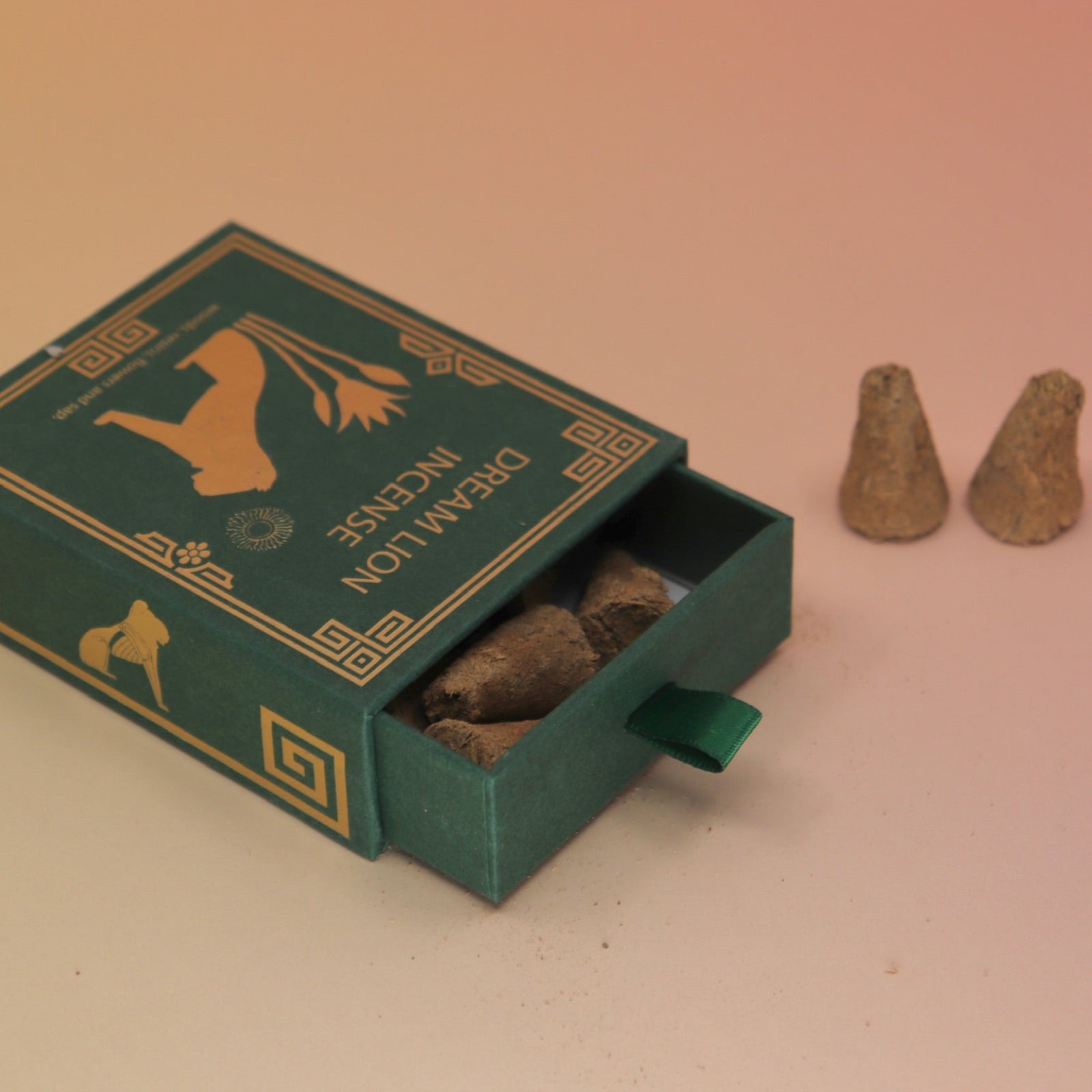 The Mayan Copal + Desert Sage Incense Cones box lying down with two cones next to it all on a pink and yellow background.