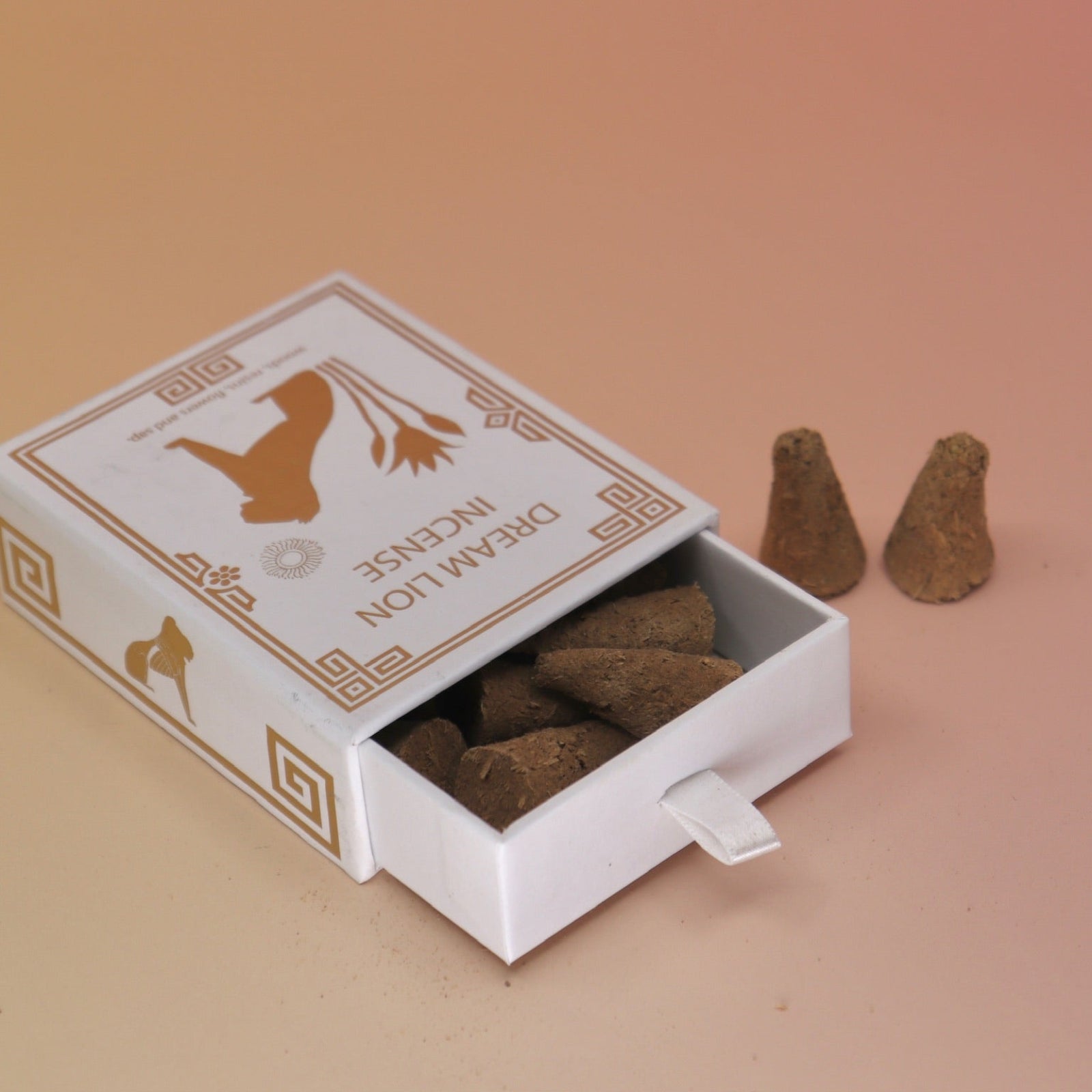 The Nine Treasures Incense Cones box lying down next to two incense cones on a pink and yellow background.