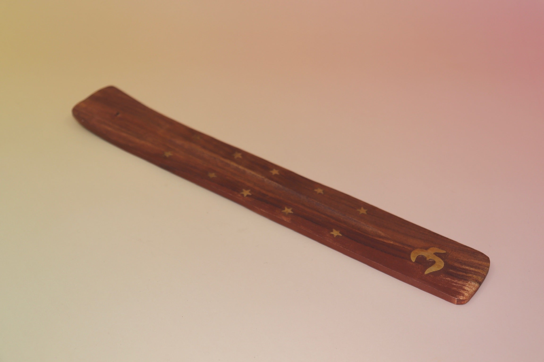 The Om Wooden Incense Burner on a pink and yellow background.