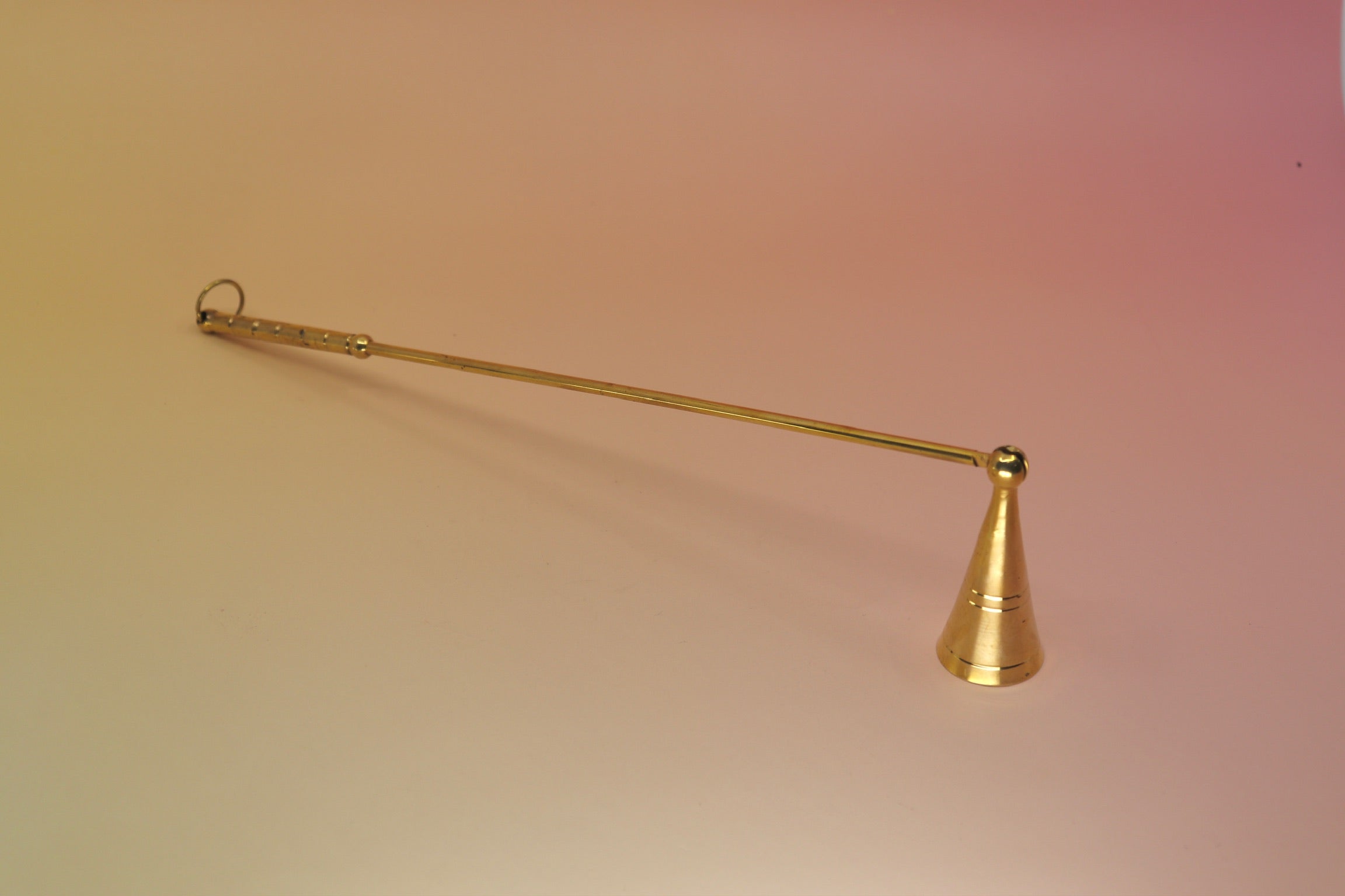 The Brass Candle Snuffer on a pink and yellow background.