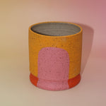 The Megan Multicolored Portal Stoneware 5 in. Planter on a pink and yellow background.
