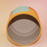 The Phoebe Multicolored Portal Stoneware 5 in. Planter on a pink and yellow background showing off the inside.