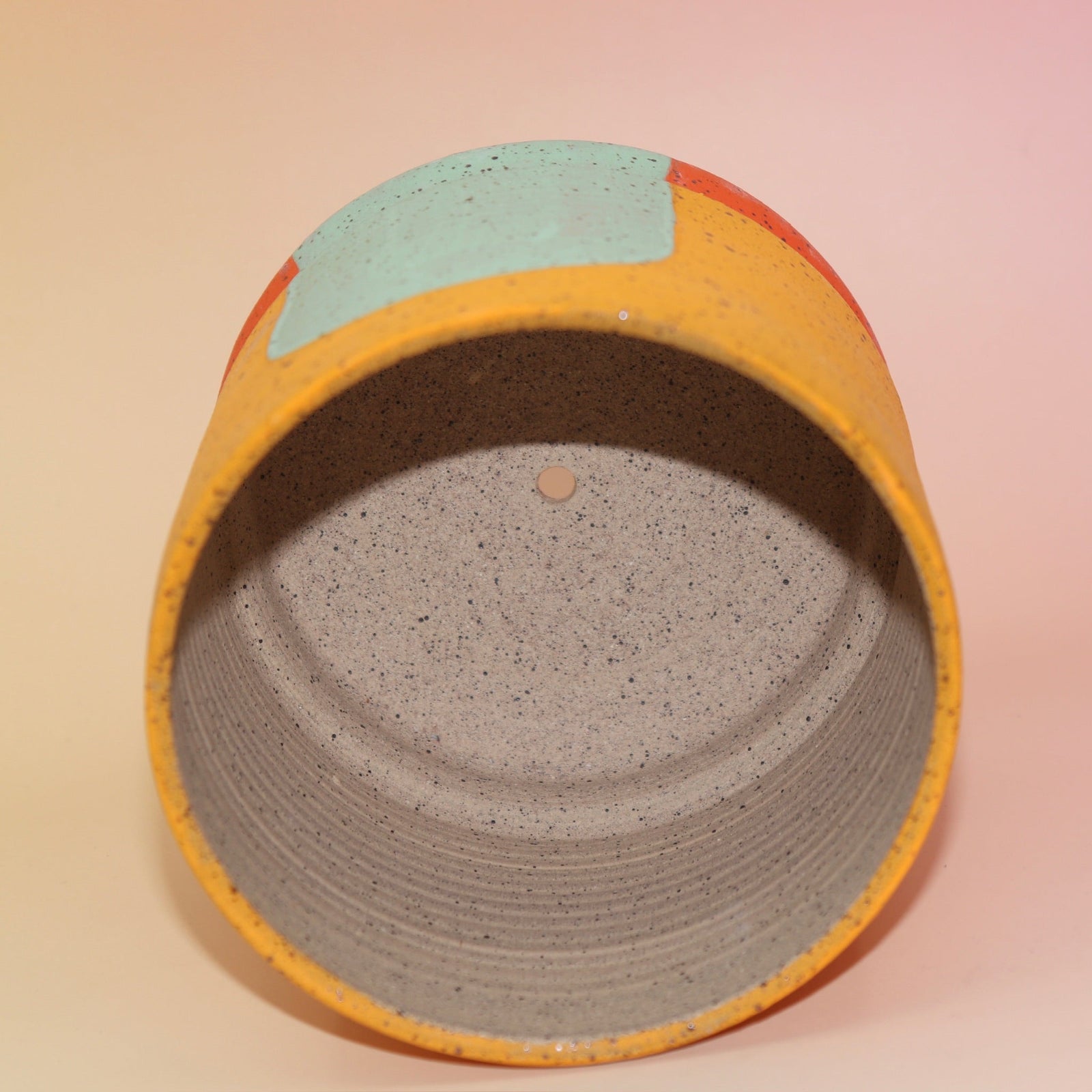 The Phoebe Multicolored Portal Stoneware 5 in. Planter on a pink and yellow background showing off the inside.