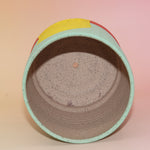 The Betty Multicolored Portal Stoneware 5 in. Planter on a pink and yellow background showing off the inside.
