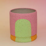 The Stacey Multicolored Portal Stoneware 5 in. Planter on a pink and yellow background.
