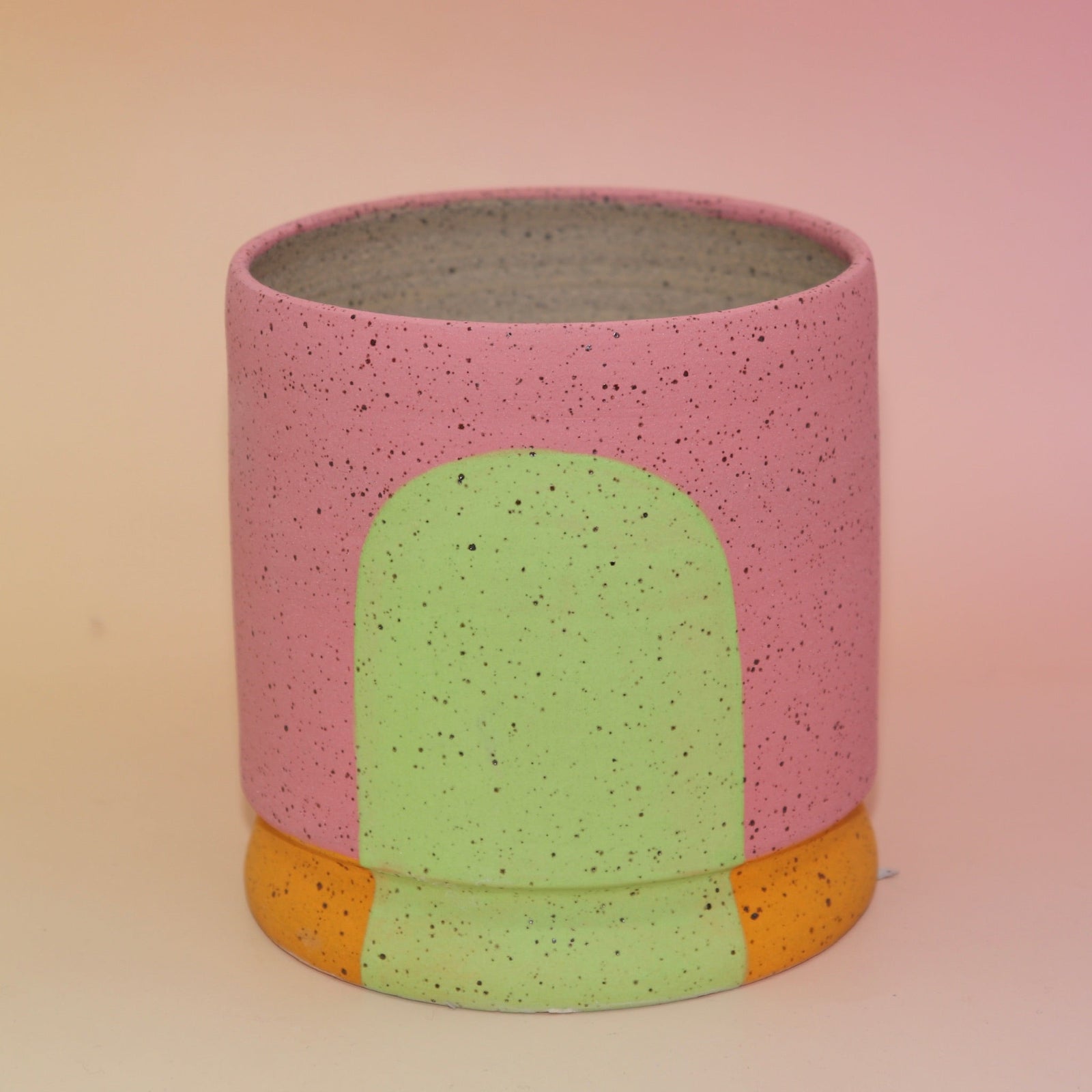 The Stacey Multicolored Portal Stoneware 5 in. Planter on a pink and yellow background.