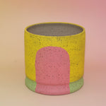 The Daisy Multicolored Portal Stoneware 5 in. Planter on a pink and yellow background.