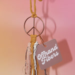 The mustard Retro Peace Sign Car Charm on a pink background.