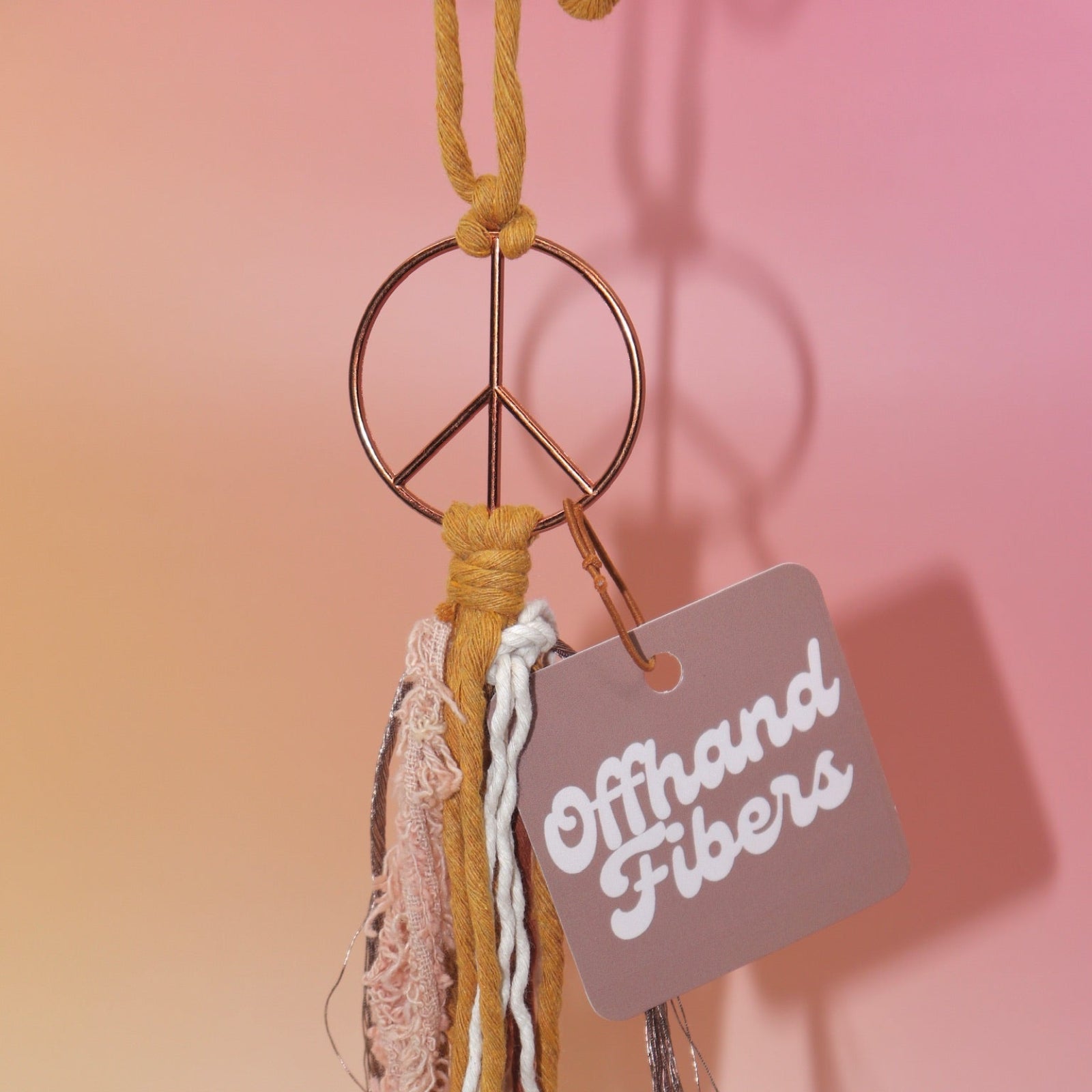 The mustard Retro Peace Sign Car Charm on a pink background.