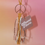 The mustard Retro Peace Sign Car Charm on a pink background.