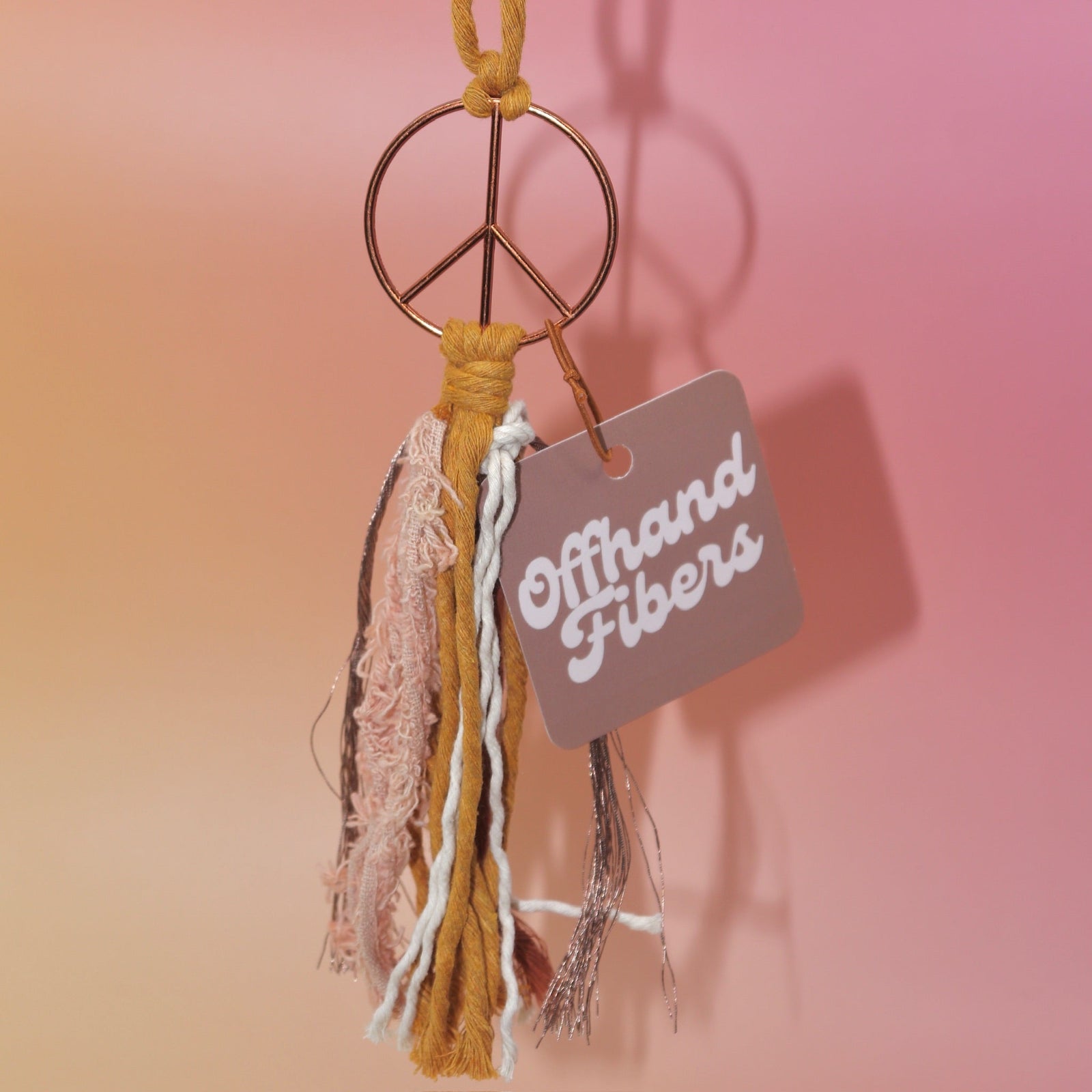 The mustard Retro Peace Sign Car Charm on a pink background.