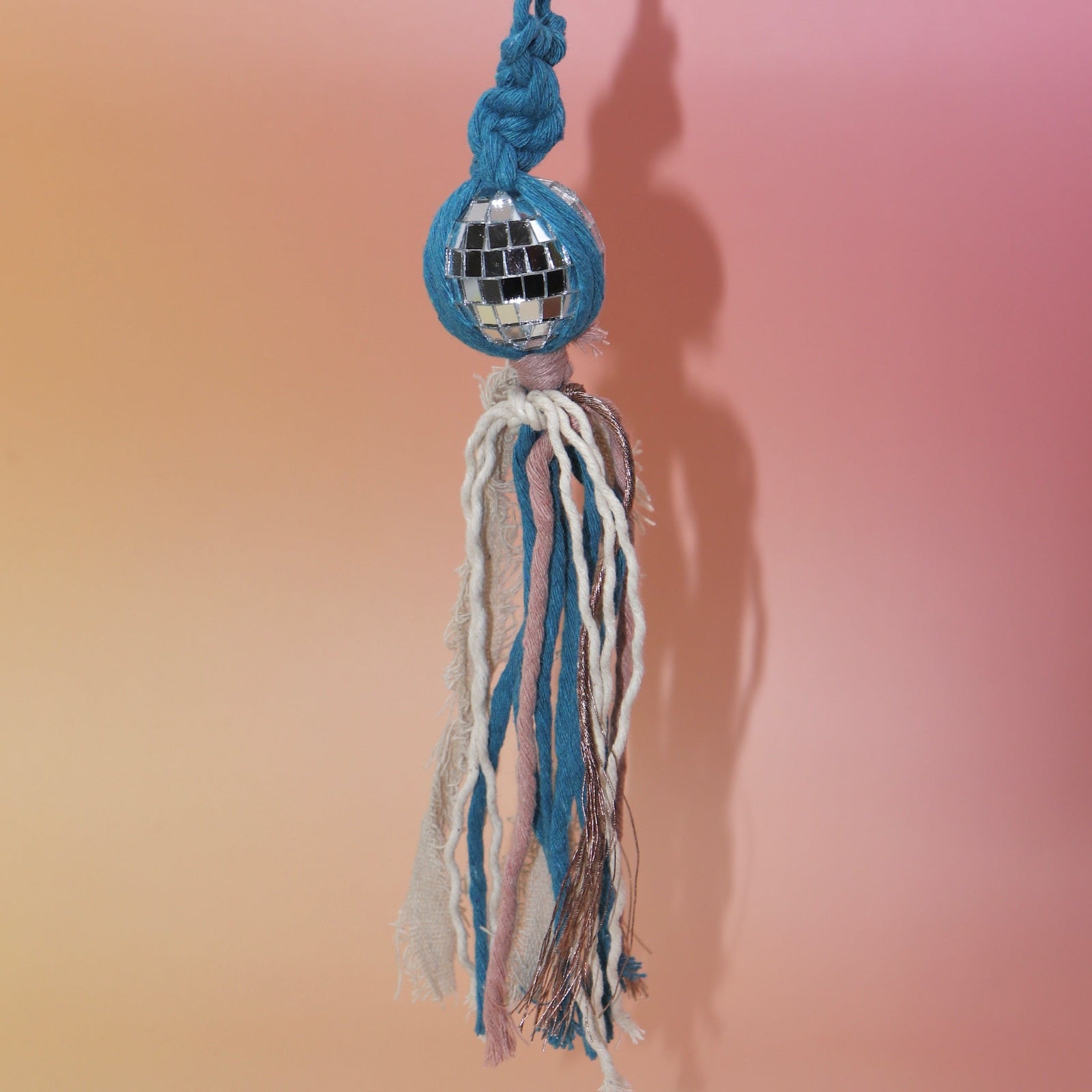 The blue Retro Disco Ball Macrame Car Charm on a pink background.