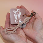 Someone holding the champagne Mini Macrame Disco Ball Keychain in front of a pink background.
