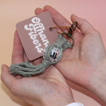 Someone holding the sage Mini Macrame Disco Ball Keychain in front of a pink background.