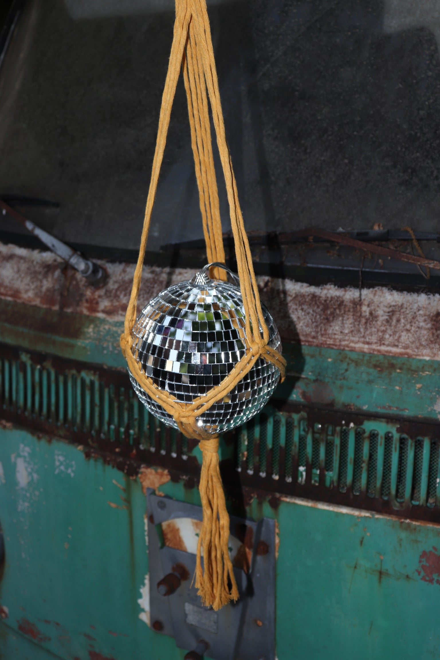 Someone holding the Mustard Disco Ball Hanger with Disco Ball in front of a vintage teal Volkswagen bus.