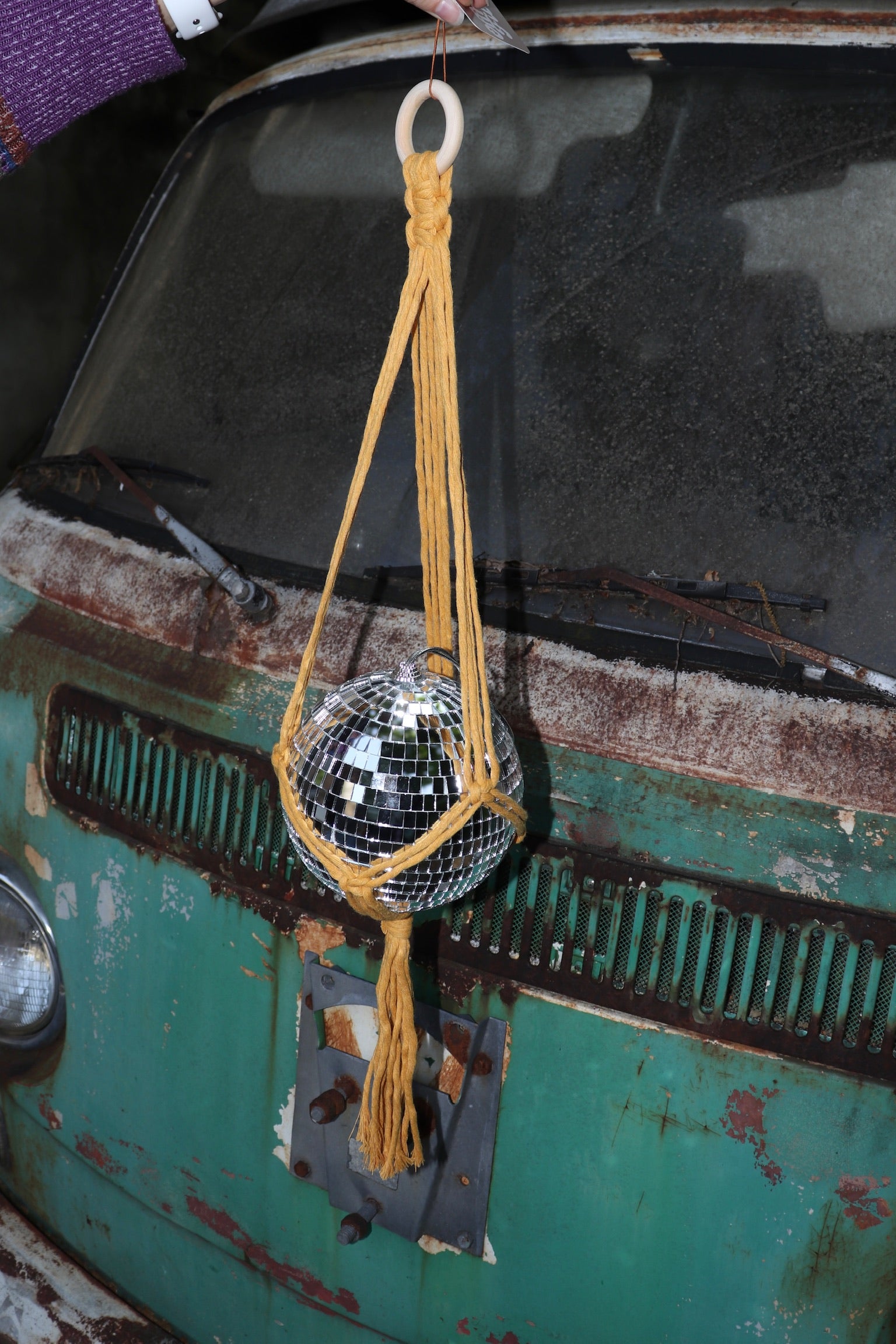 Someone holding the Mustard Disco Ball Hanger with Disco Ball in front of a vintage teal Volkswagen bus.