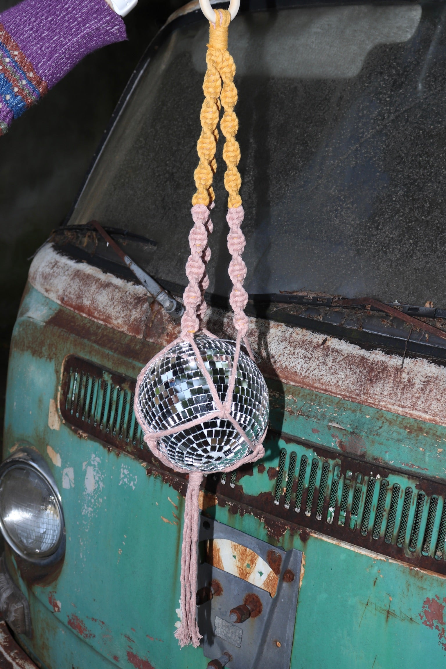 Someone holding the blush and mustard Color Dip Disco Ball Hanger - Macrame Plant Hanger in front of a vintage teal Volkswagen bus.