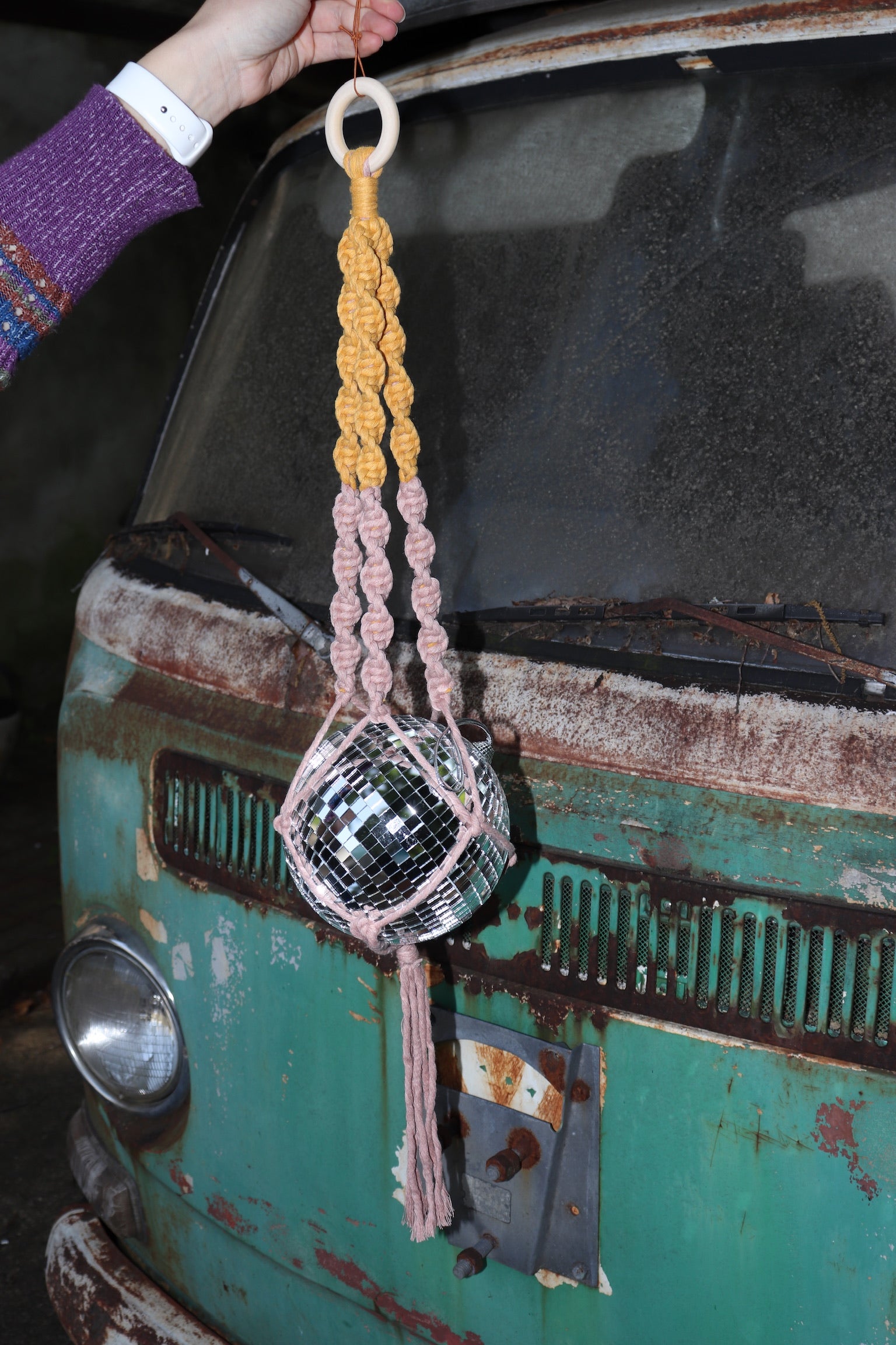 Someone holding the blush and mustard Color Dip Disco Ball Hanger - Macrame Plant Hanger in front of a vintage teal Volkswagen bus.