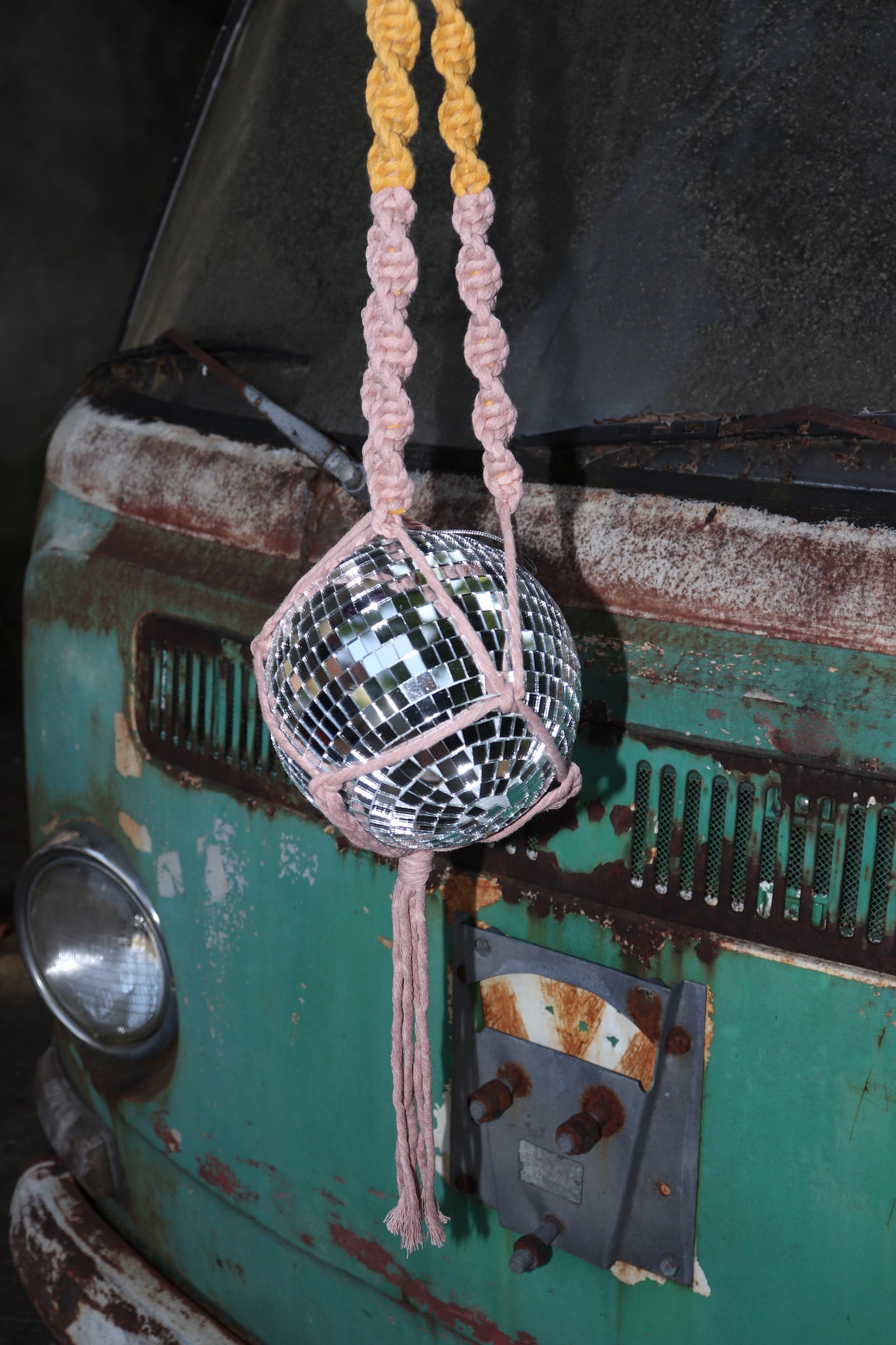 Someone holding the blush and mustard Color Dip Disco Ball Hanger - Macrame Plant Hanger in front of a vintage teal Volkswagen bus.