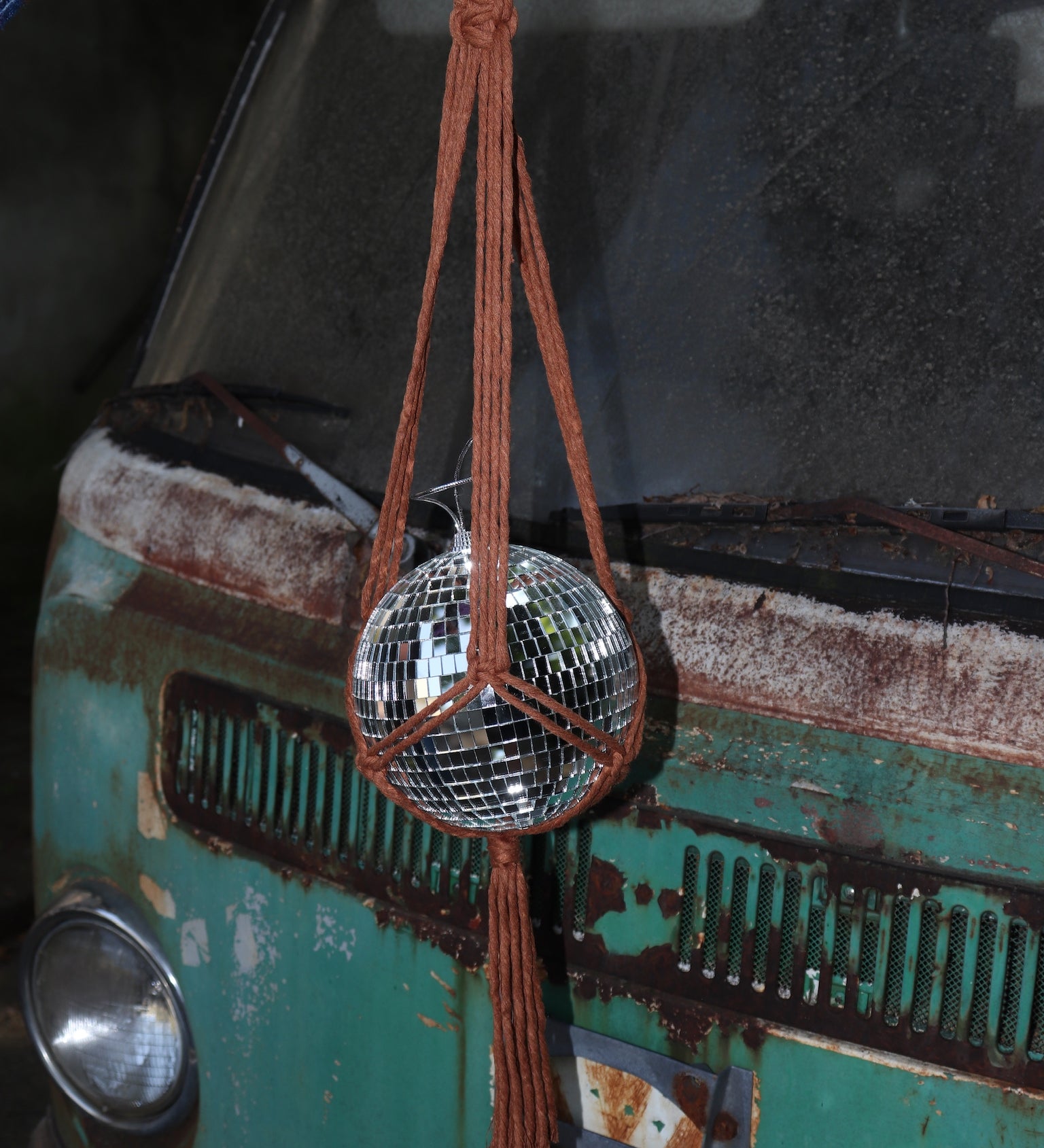 Someone holding the Rust Disco Ball Hanger with Disco Ball in front of a rusted teal Volkswagen bus.