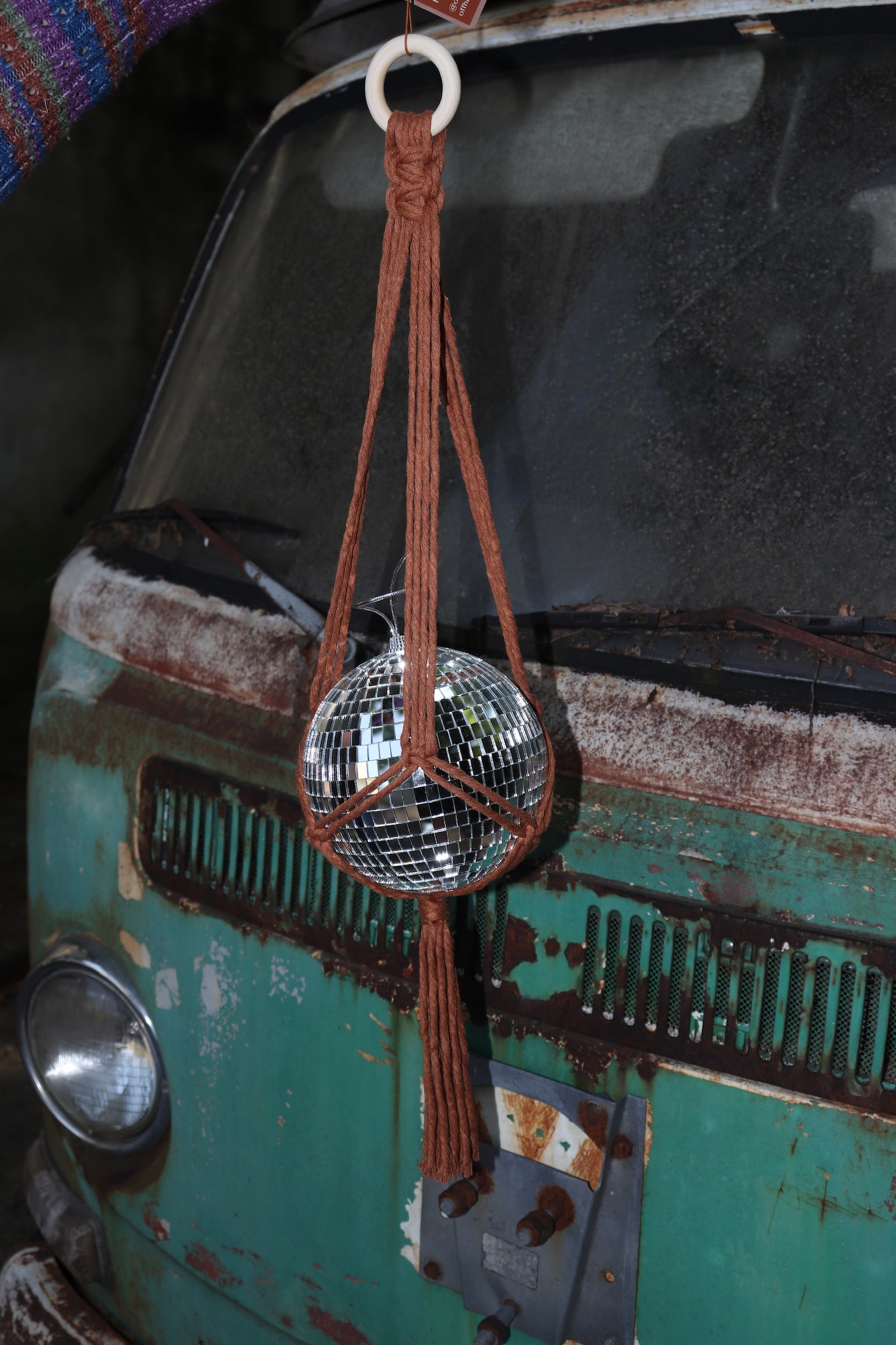 Someone holding the Rust Disco Ball Hanger with Disco Ball in front of a rusted teal Volkswagen bus.