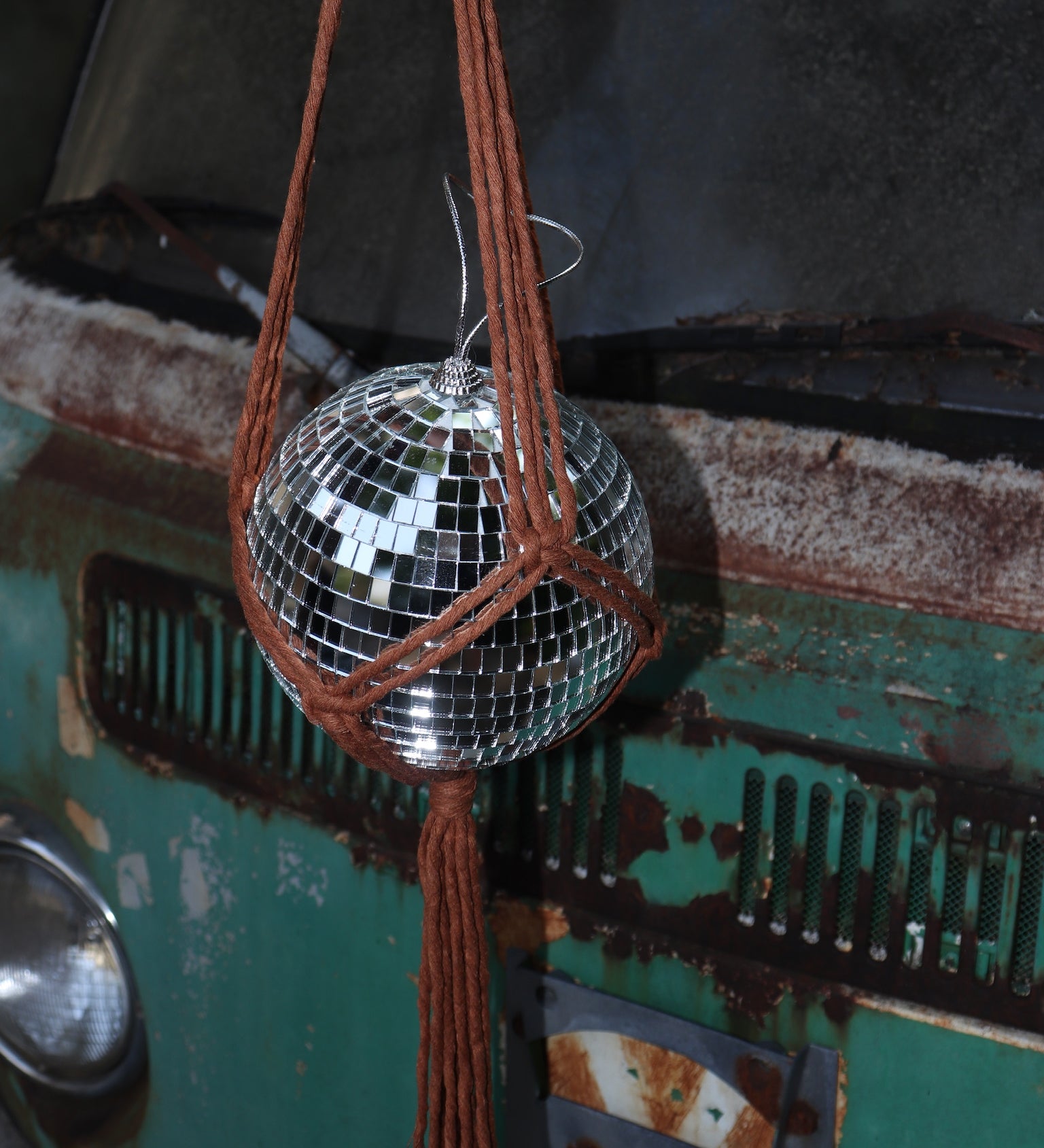 Someone holding the Rust Disco Ball Hanger with Disco Ball in front of a rusted teal Volkswagen bus.