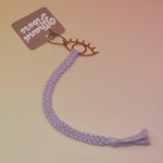 The lavender All Seeing Eye Charm Macrame 12 in. Bookmark on a light pink and yellow background.