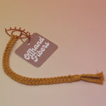 The mustard All Seeing Eye Charm Macrame 12 in. Bookmark on a light pink and yellow background.