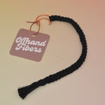 The black Boho Moon Charm Macrame 12 in. Bookmark on a light pink and yellow background.
