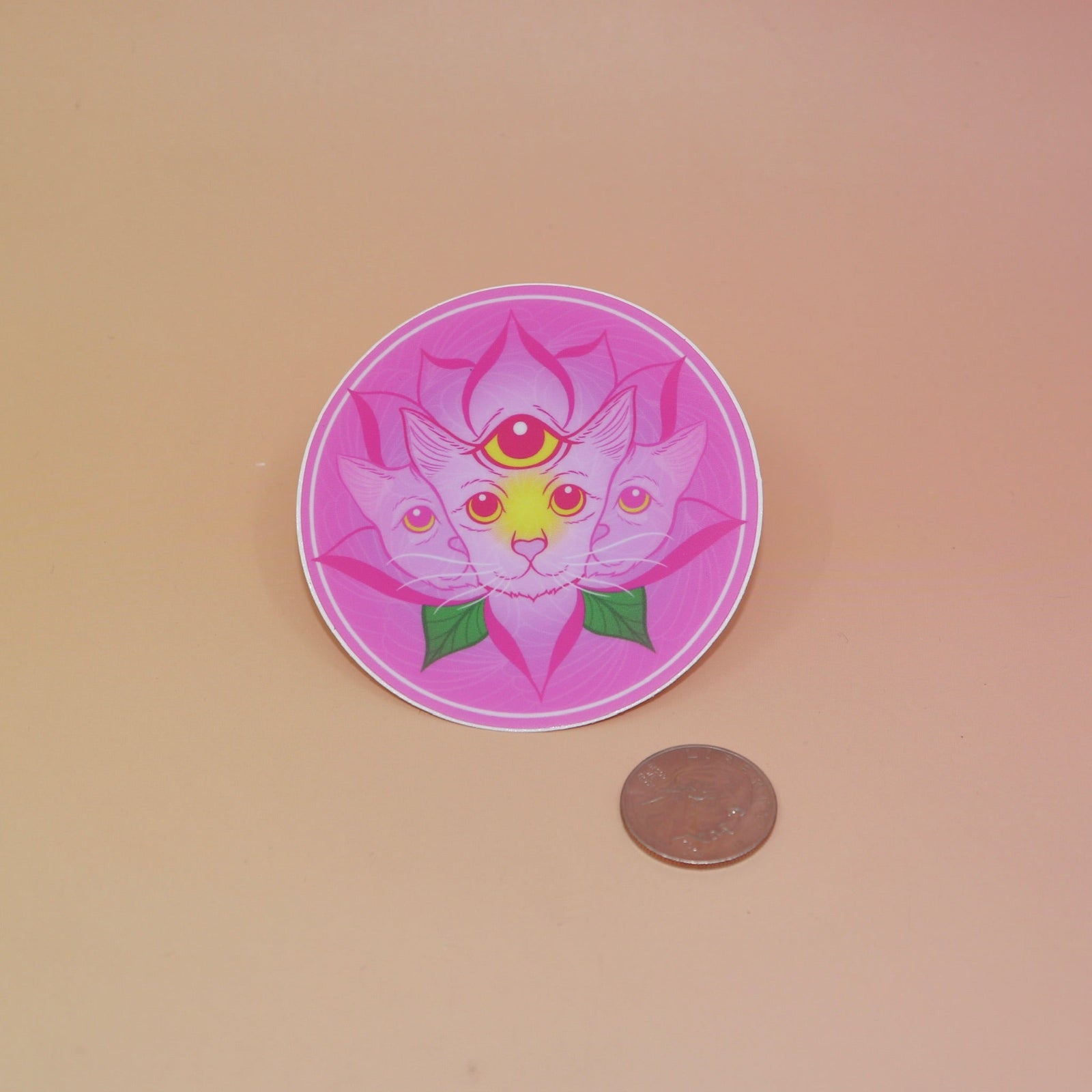 The Four Eared Lotus 3” Round Vinyl Sticker next to a quarter on a light pink background.