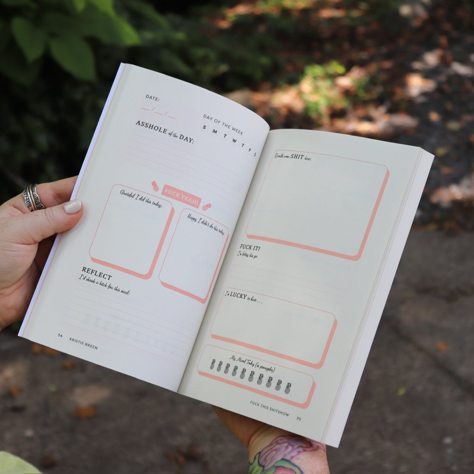 Someone holding the F*ck This Sh*tshow Gratitude Journal open to show off the pages.