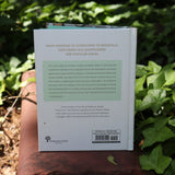 The Ritual Wellness Adaptogens - Herbs for Longevity and Everyday Wellness Book on a red brick surrounded by green ivy.