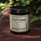 The back of the Happiness Herbal “Coffee” Powder on a rusty red surface surrounded by green ivy.