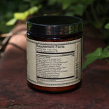 The back of the Golden Sun Milk - 5oz Energizing Adaptogenic Chai Powder on a red surface next to ivy.
