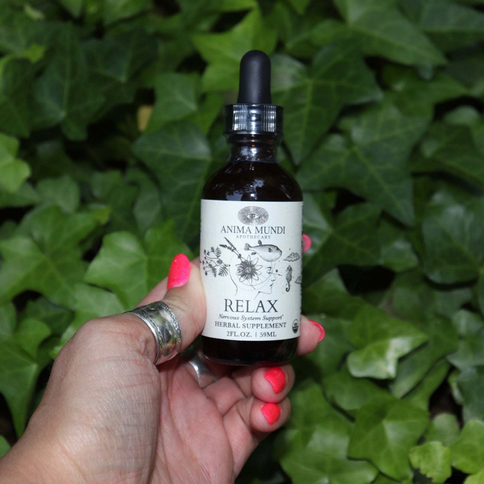 Someone holding the Relax - Nervous System Support Tonic in front of a patch of ivy.