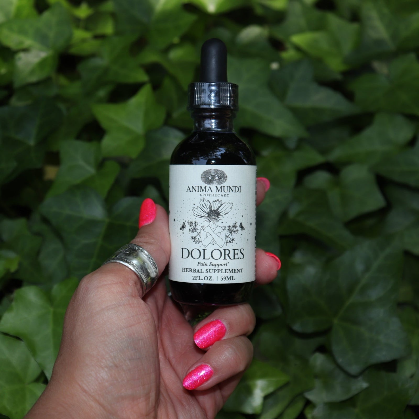 Someone holding the Dolores - Muscular Comfort + Nerve Support Tonic in front of a patch of ivy.
