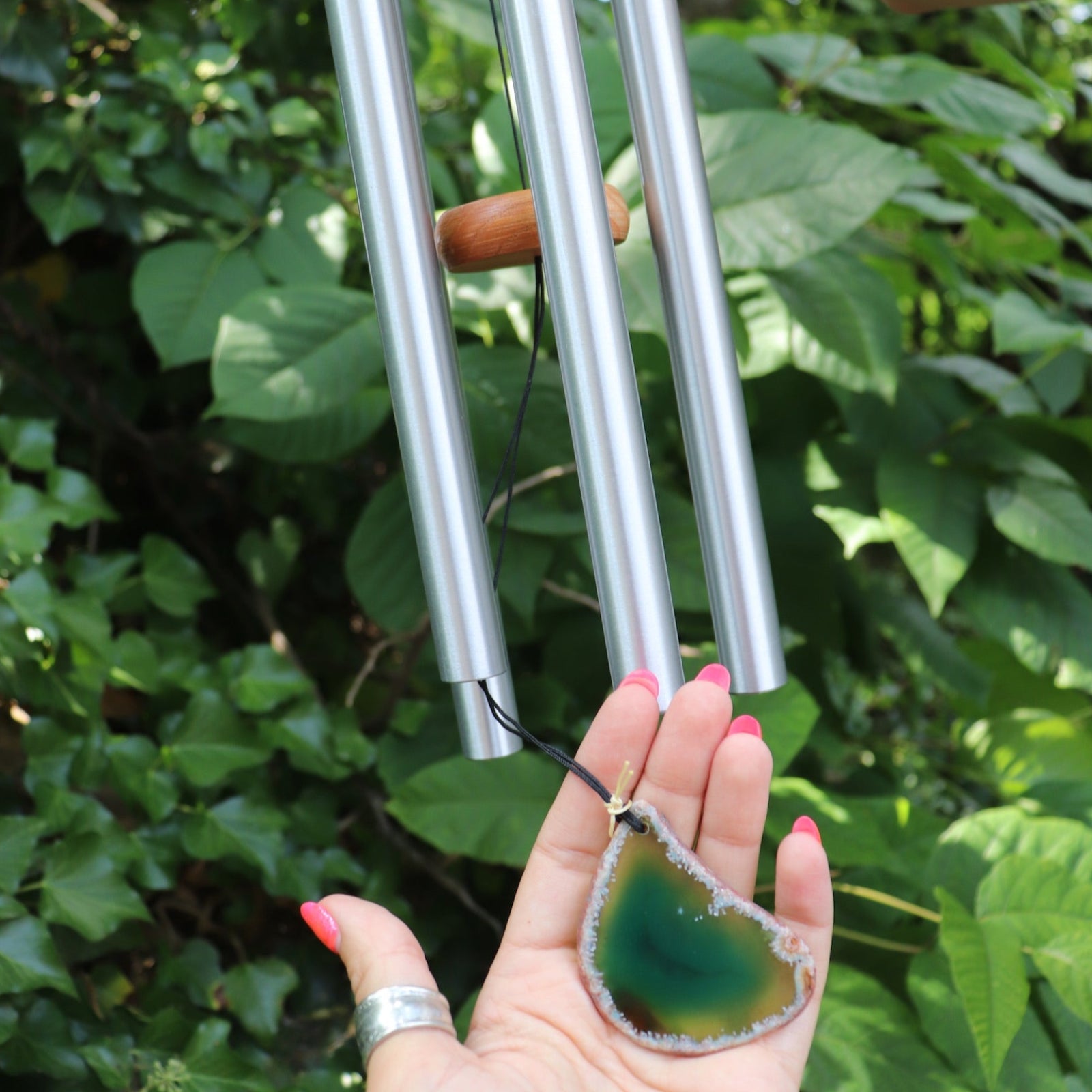 Someone holding the agate slice from the Woodstock Agate Celtic Chime in front of bushes.