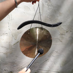 Someone holding the Woodstock Hand-Hammered Brass Hanging Gong in front of a white wall.